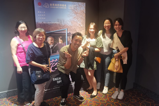 Director He Shuming taking photos with audience members in front of the movie poster. 
