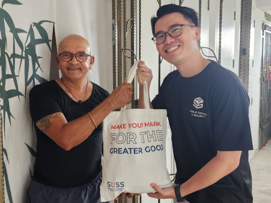 Brenban Lim, Vice-Chairperson of SUSS Public Safety and Security Interest Group smiles graciously as he gives the donation bag to a resident.