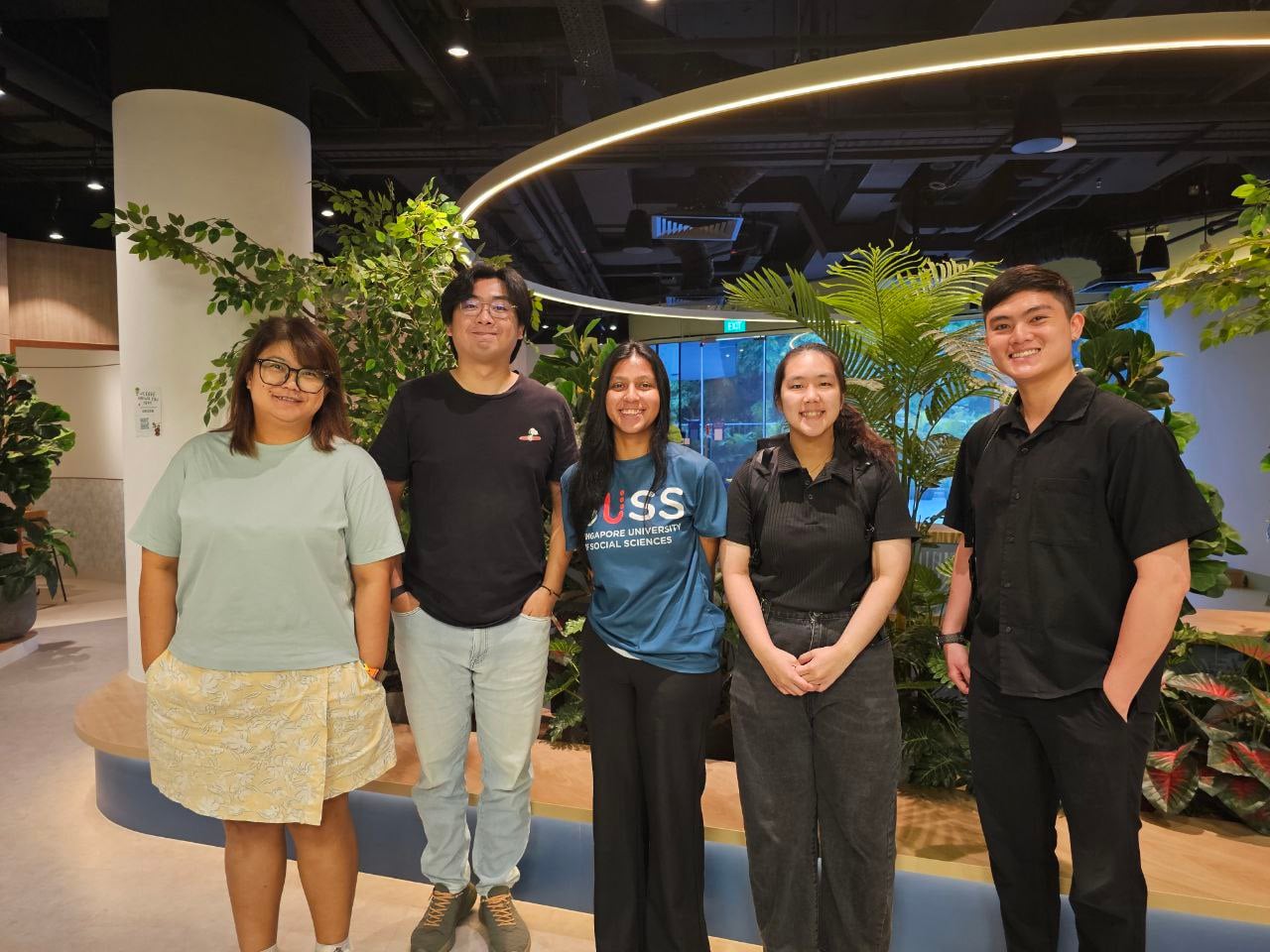 Four individuals stand together in front of a vibrant plant display, showcasing various types of greenery and flowers