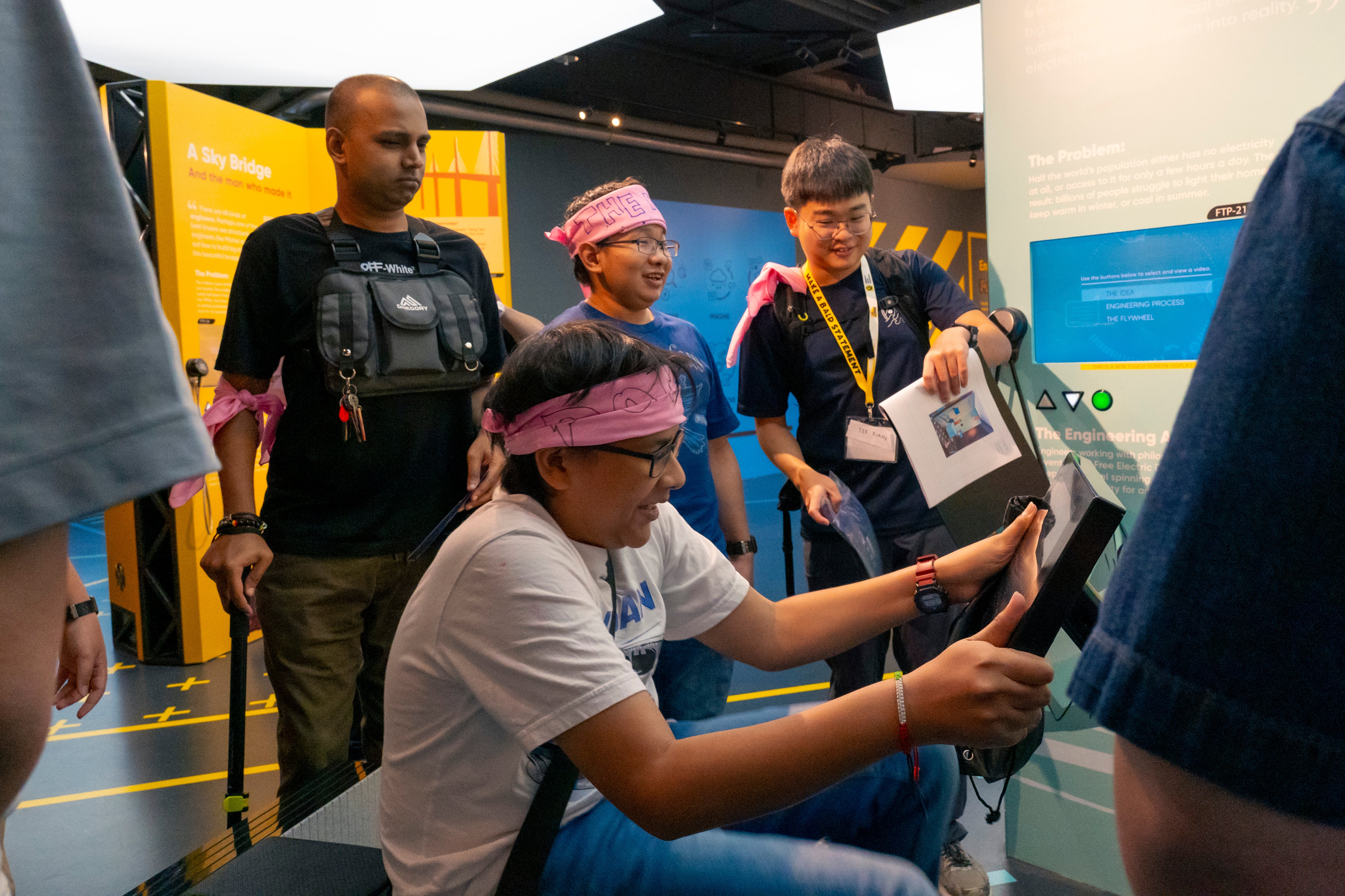At one of the Amazing Race stations, a beneficiary pedals on a stationary bike to generate electricity and clear the challenge, as Wo