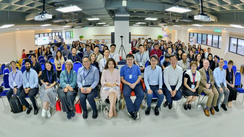 Group photo of a diverse team in an office setting with rows of people seated and smiling