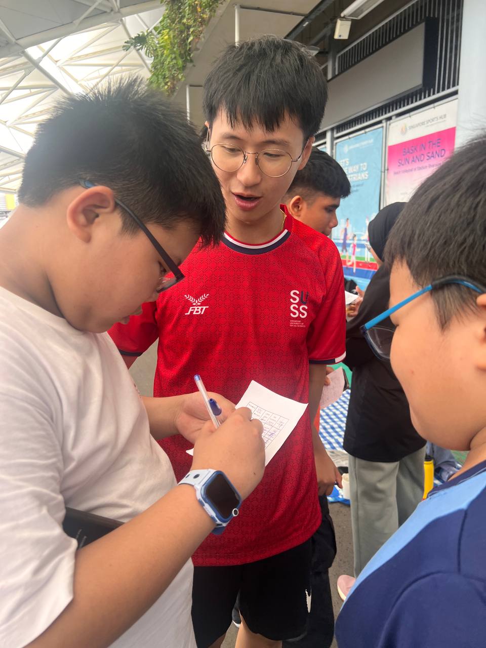 Guiding two boys through the icebreaker bingo game, Lee Hao helps spark conversation and connection as they mark off their cards