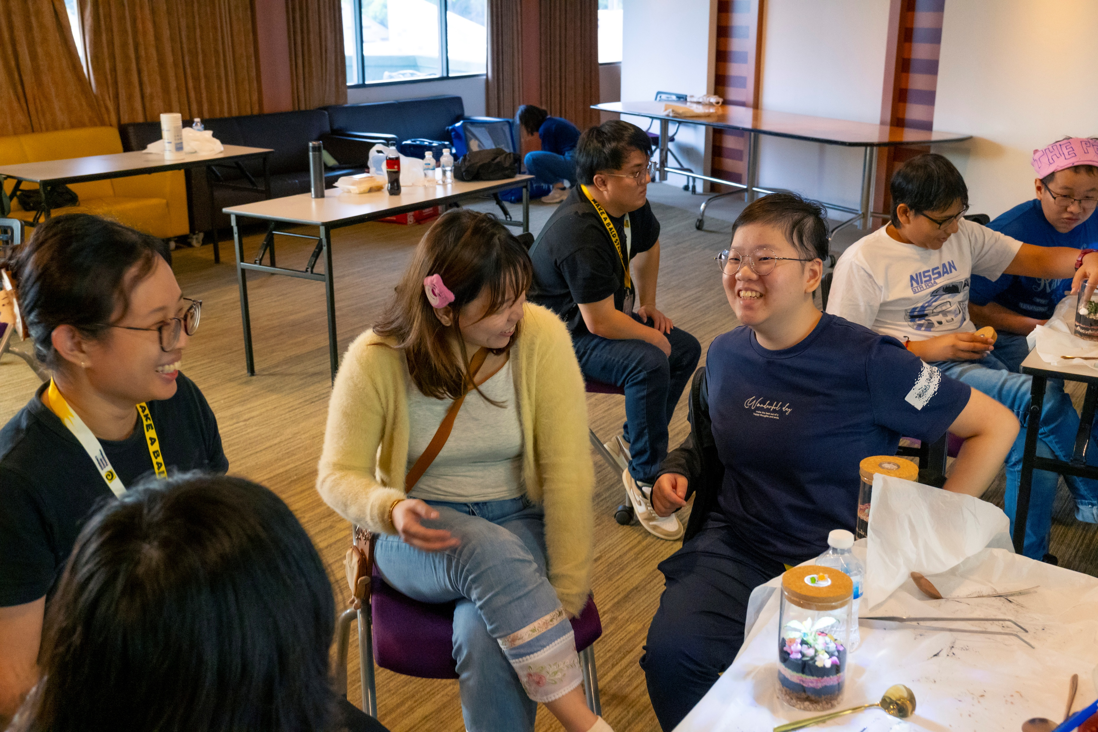 Isabella Leow Pei Jin sits with a beneficiary and another member, smiling and chatting as they enjoy the terrarium workshop.