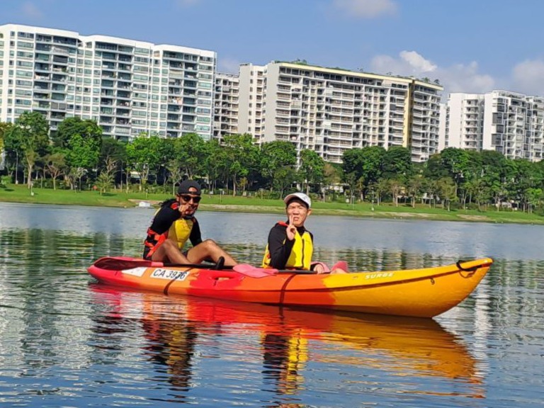 M. Presanth points to the camera with a smile while the MINDS client flashes a peace sign, both enjoying a lighthearted moment on the water during their kayaking session.