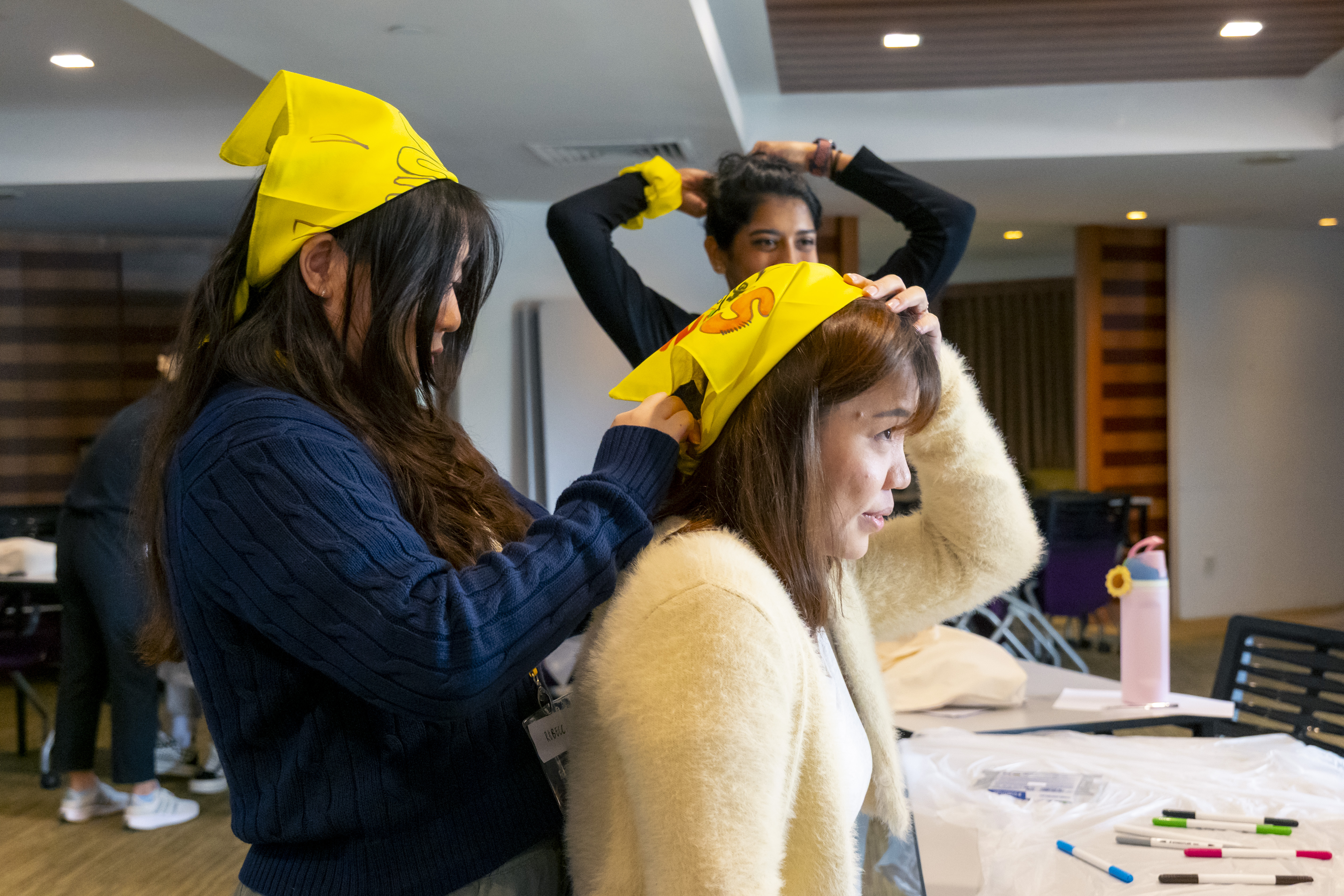 Rebecca Koh helps a teammate tie her yellow bandana on her head, featuring the group name and hand-drawn logo created by the team.