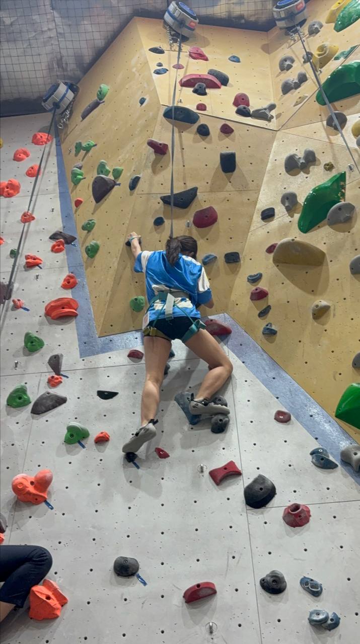 ngel Ng Yi Ting climbs a route on the high wall at Outpost Climbing gym, demonstrating focus and determination while embracing the challenge of the activity.