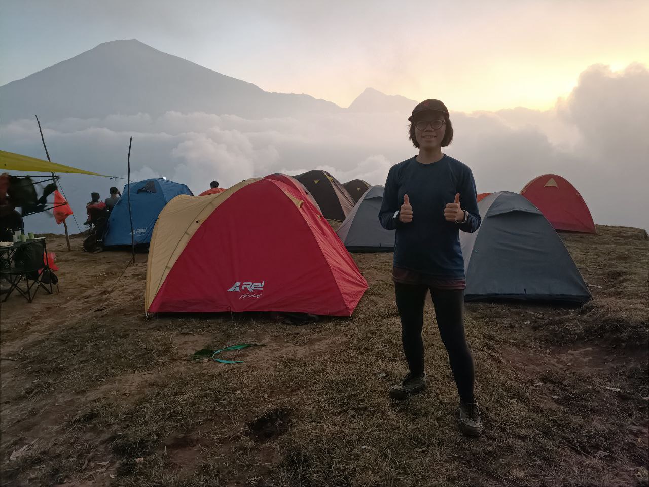 Deborah Seah posing at Pergasingan Hill with the tents set up for the night behind her and Mount Rinjani in the background.