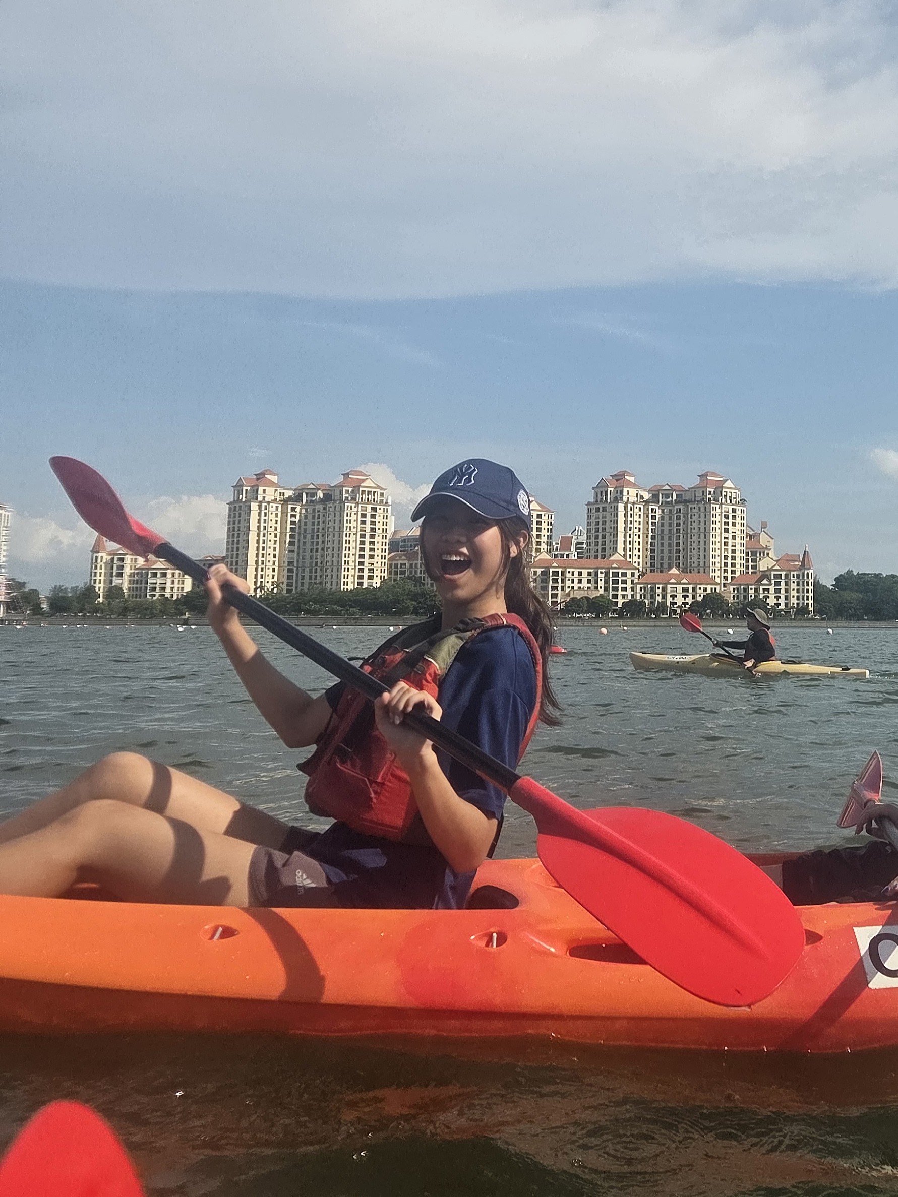 Chloe Lim Yu En smiles for the camera while kayaking, holding her paddle up and enjoying the moment on the water.