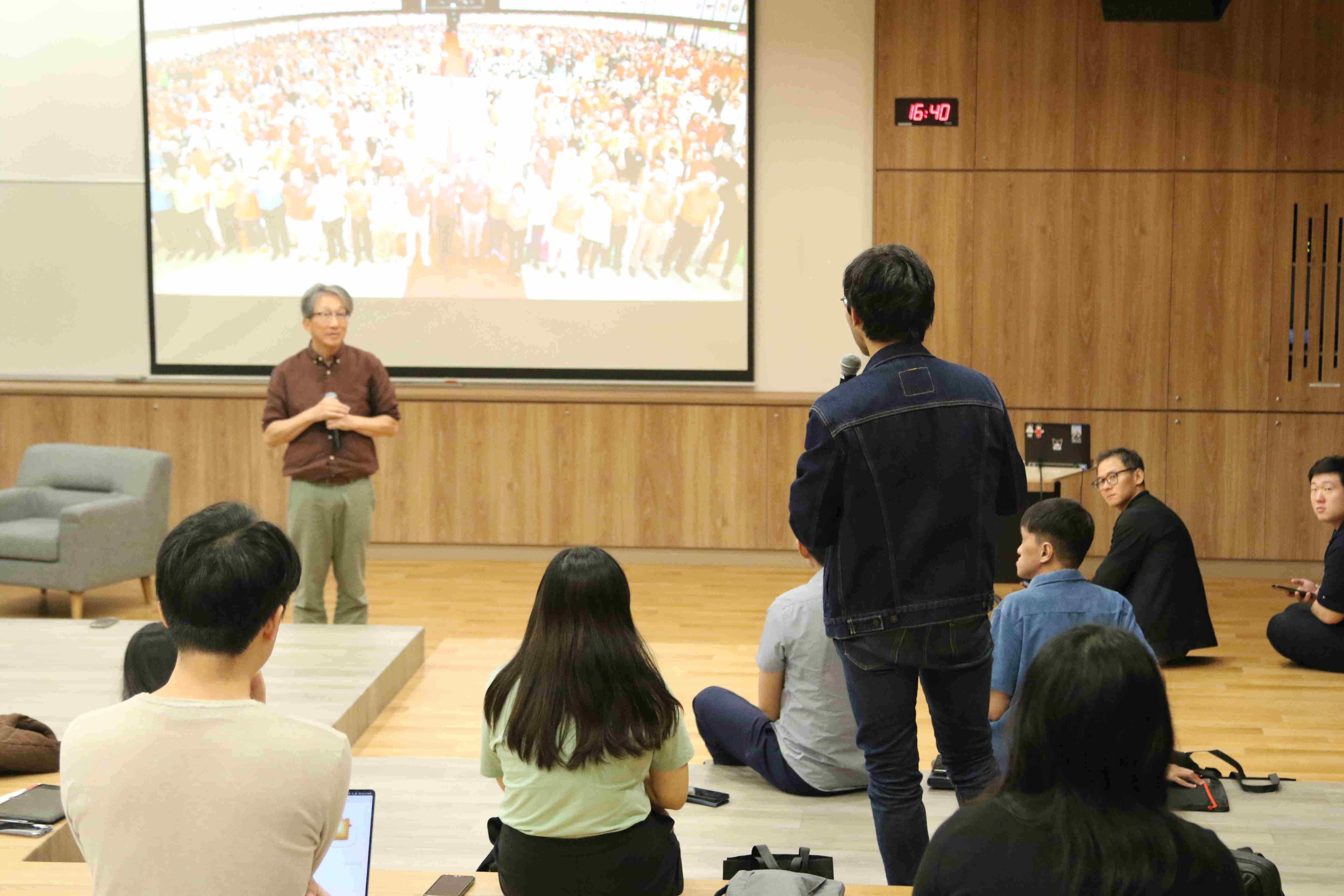 Speaker and audience in a lecture hall with a large s