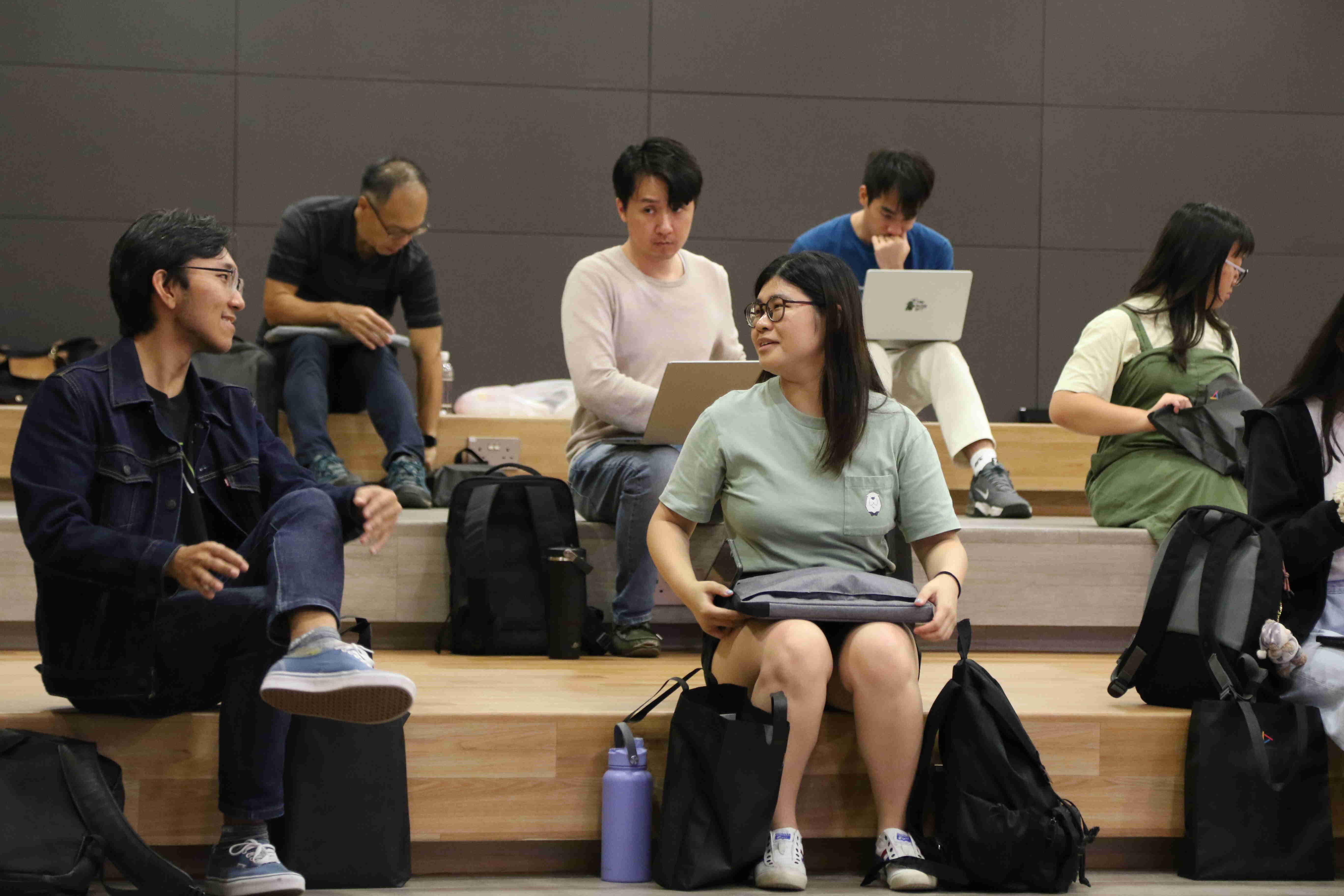 Students sitting on tiered seating with laptops and backpacks