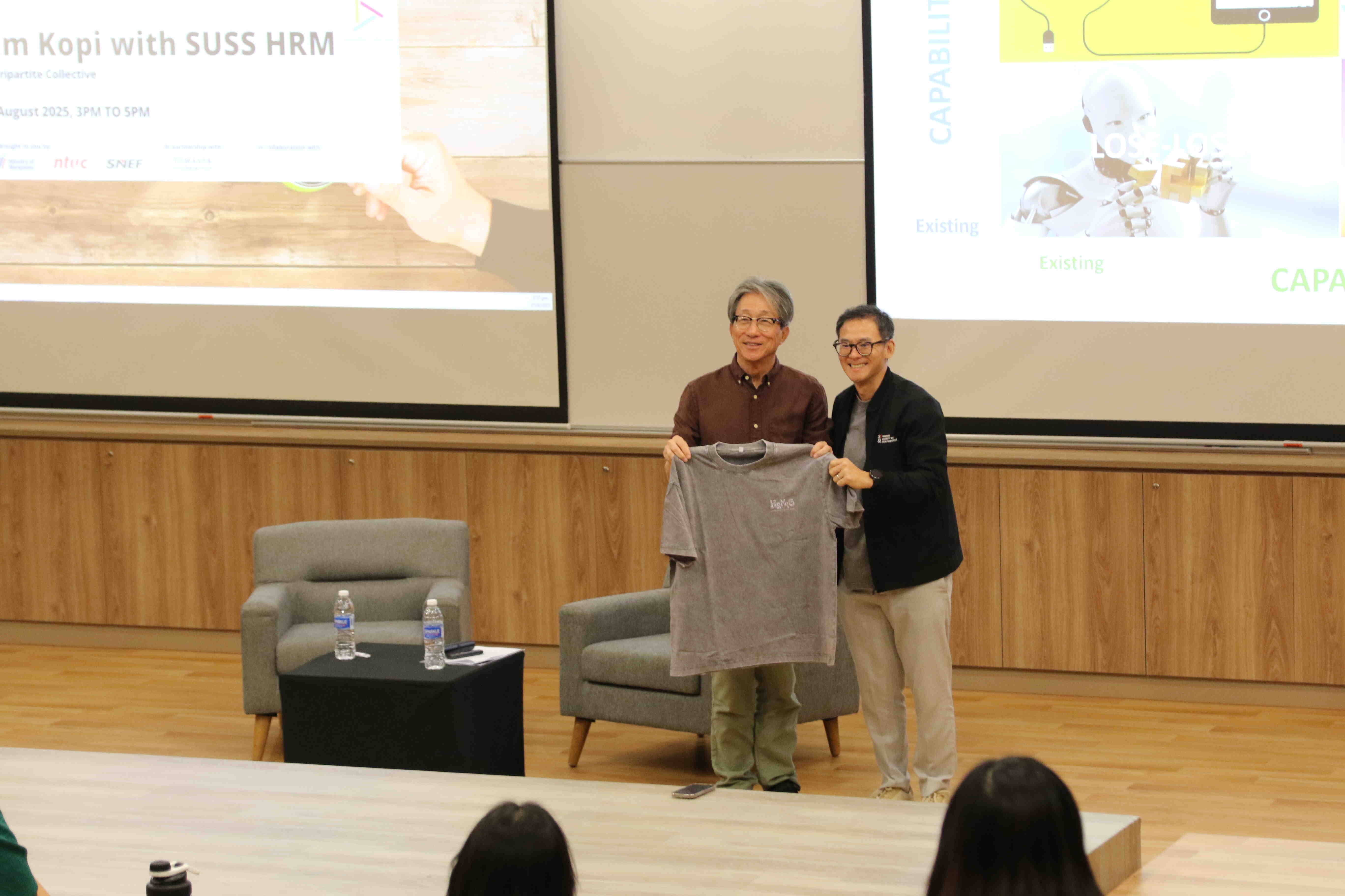Two people holding a t-shirt in front of a presentation