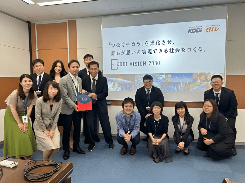 People posing for a photo with KDDI presentation at the back