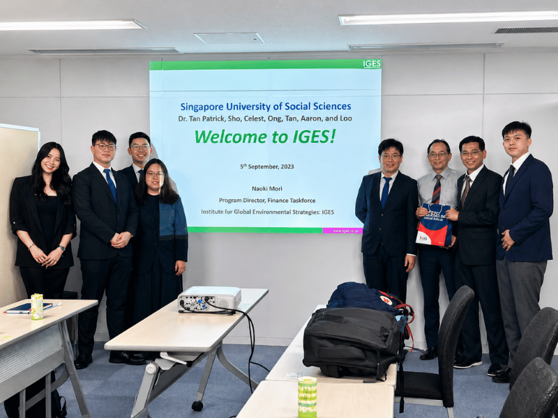 Group of people in suits posing for a photo in front of a screen that says "Welcome to IGES!"