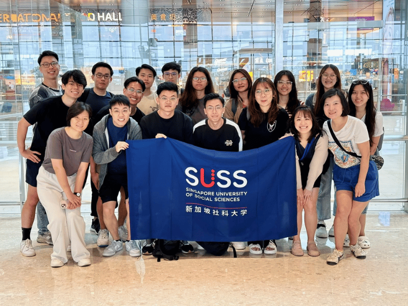 Group of people posing for a photo holding a SUSS school banner