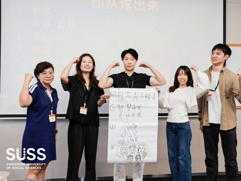 5 people posing with their arms up with a sheet of paper in front of the middle person with Chinese words on the paper