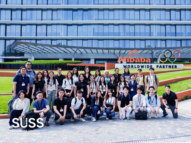 Group of people posing in font of Alibaba Logo